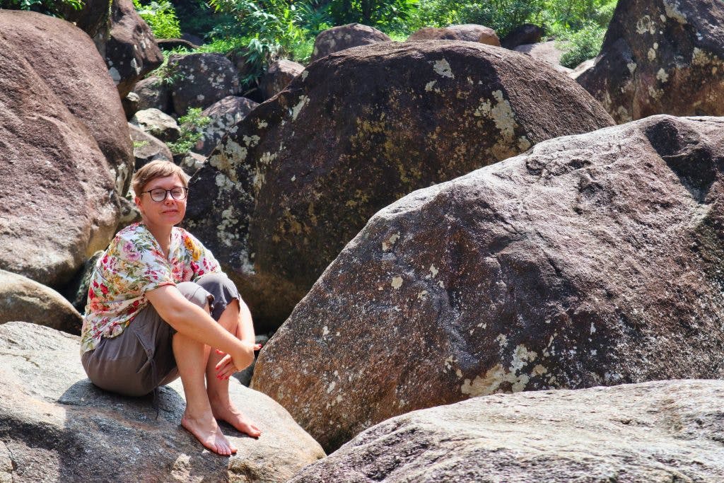 a woman sitting on a rock at promlok waterfall