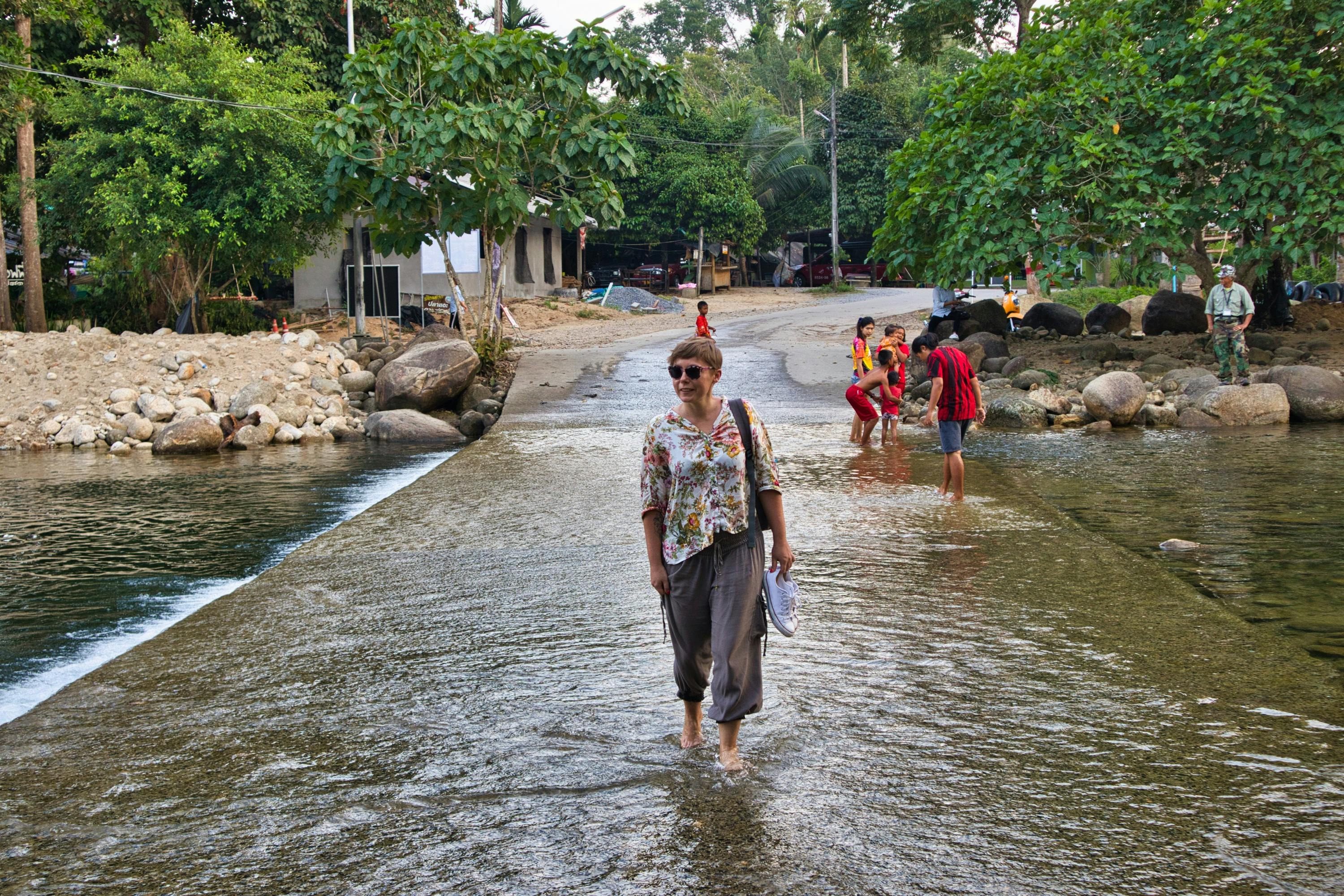 a woman dressed in a flowery shirt walks through the stream in thailand
