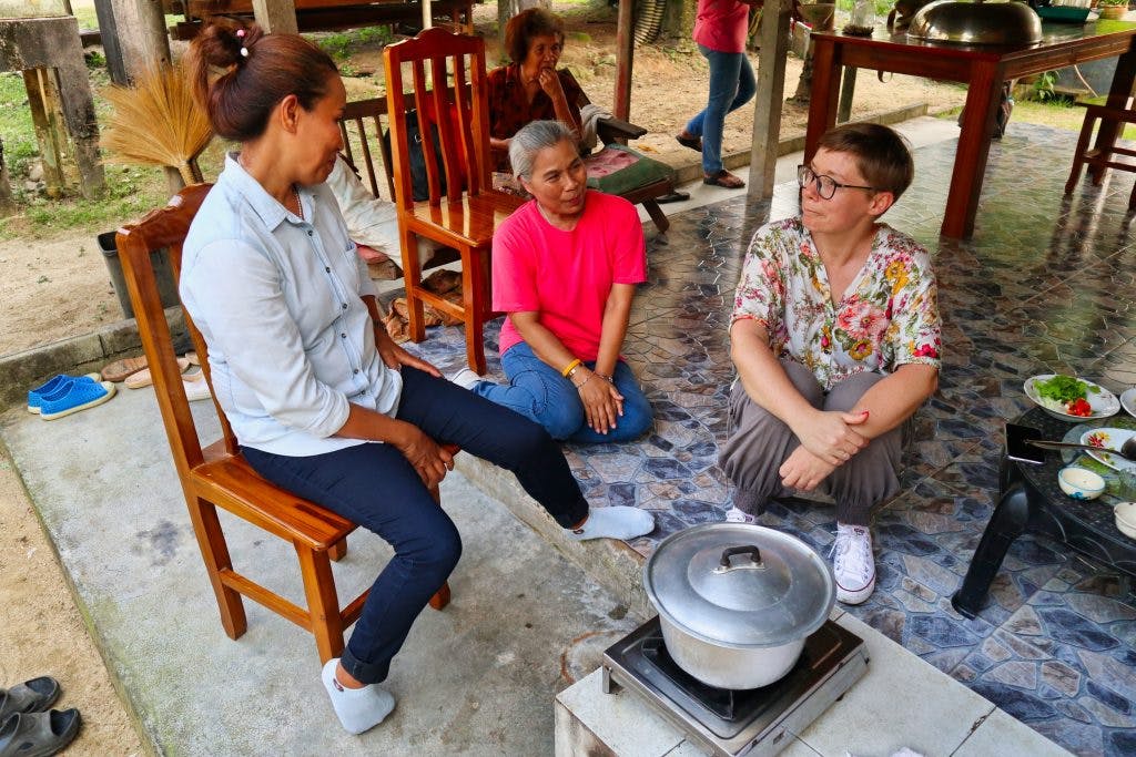 Two thai women talking to a tourist while cooking in a Thai village in nakhon si thammarat province. 