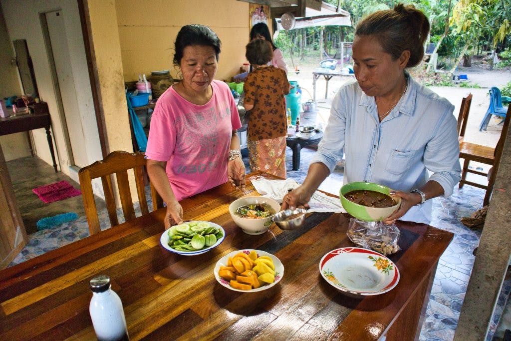 two thai women in the countryside are preparing food and setting it up on the table