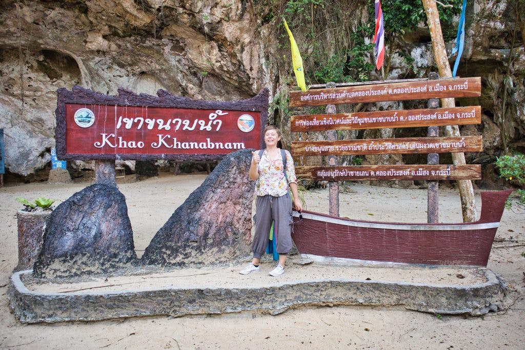 a woman stands in front of a sing at kanabnam cave, krabi province