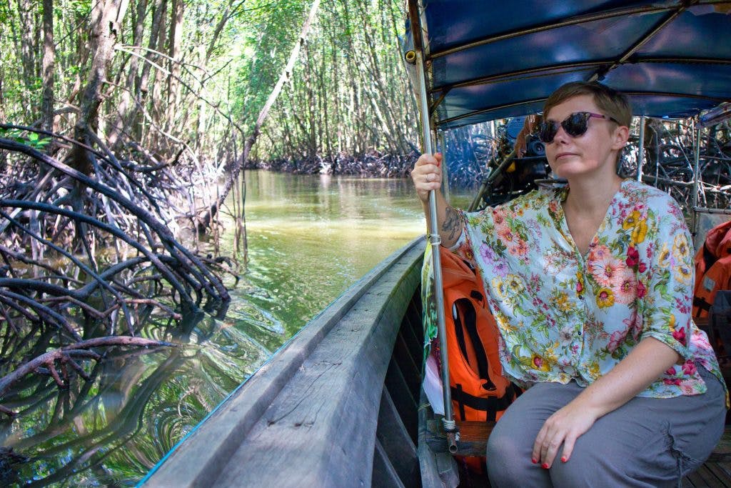 A woman sitting in a long tail boat sailing through mangrove forest in krabi, thailand. 