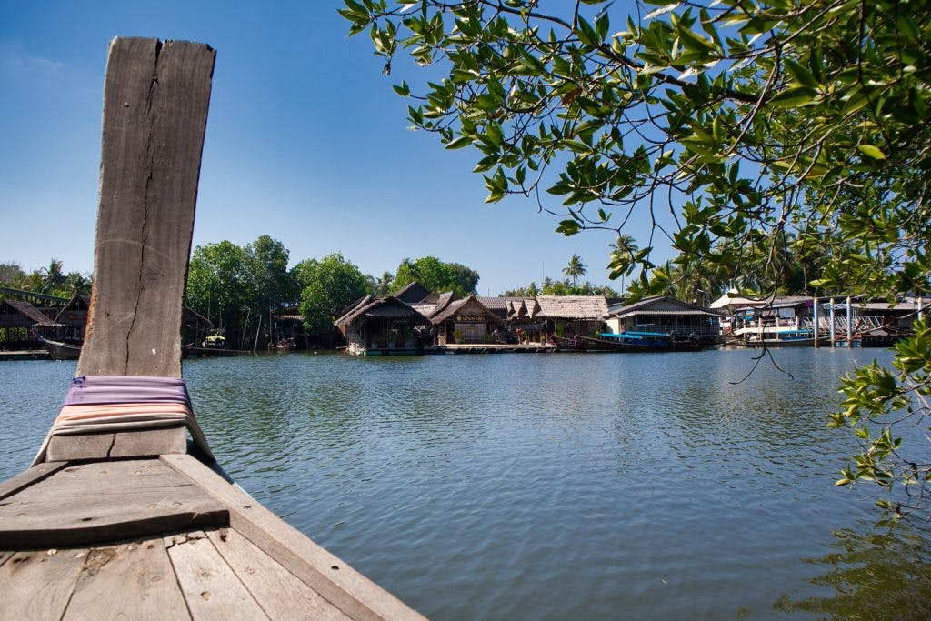 rząd chatek z bambusa widzianych z długiej, drewnianej łódki w Tajlandii. 