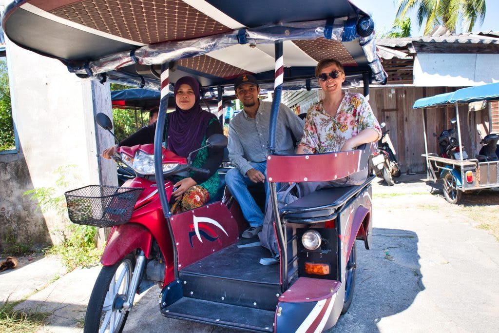 a muslim woman driving a rickshaw with two passangers in krabi, thailand. 