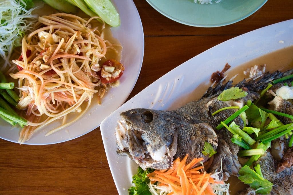 papaya salad and fish on a plate in a restaurant on koh klang, thailand. 