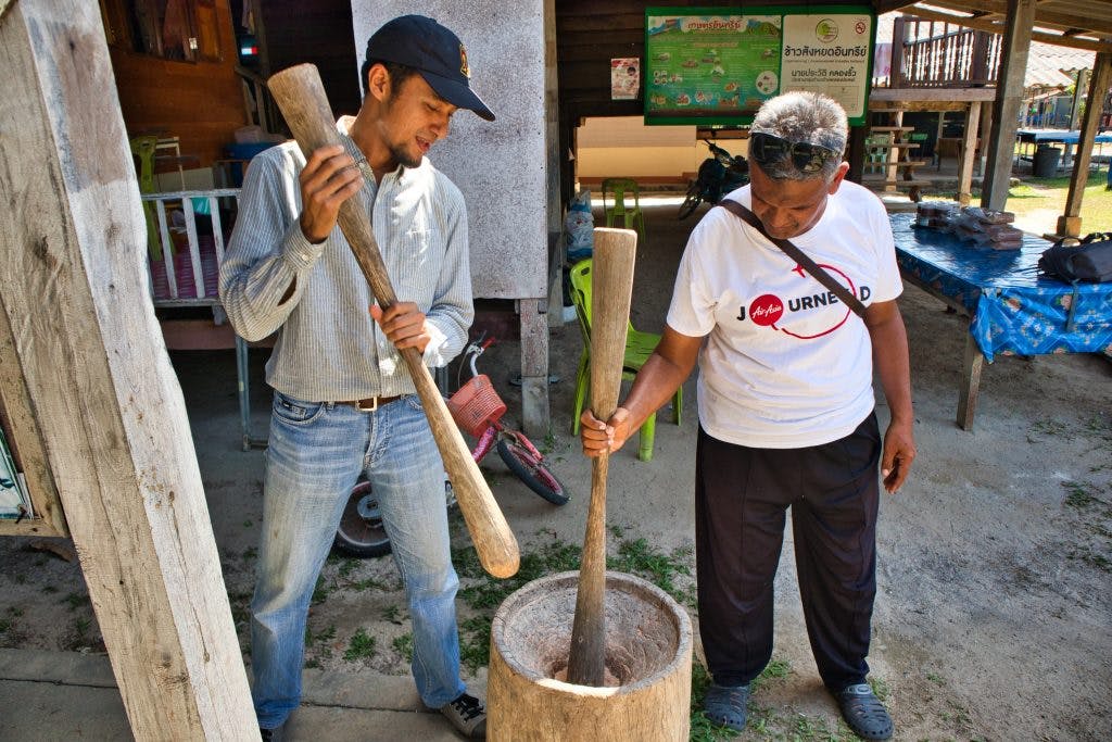two Thai men are making rice with old tools. 