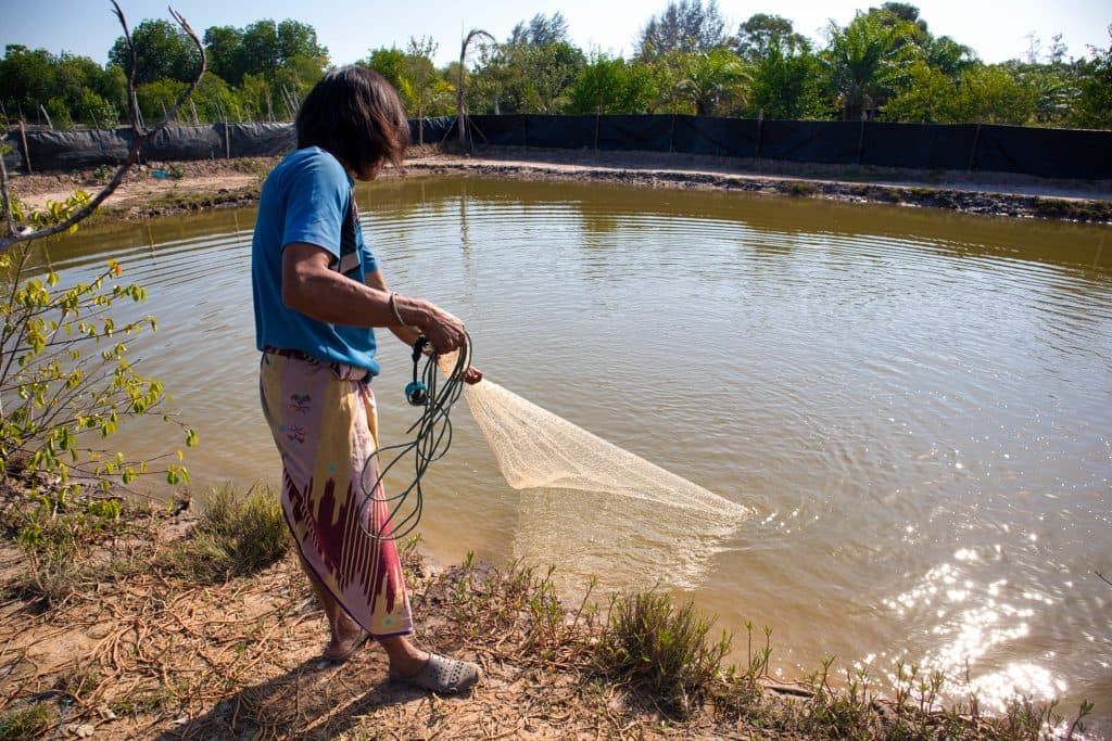 a thai man dressed in a sarong fishing at a small pond on koh klang, krabi, thailand.