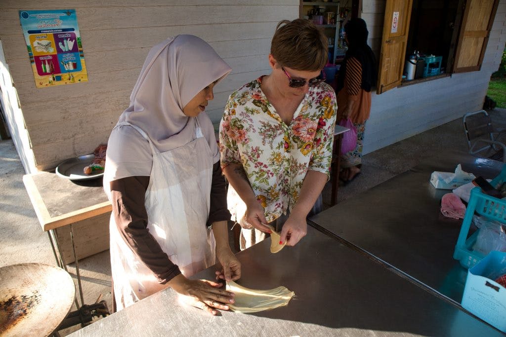 muzułmanka w szarej chuście pomaga turystce zrobić roti. 