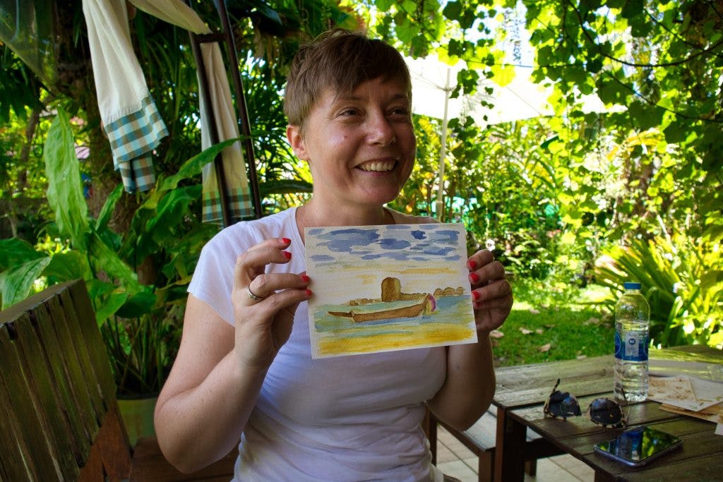 kobieta trzyma w rękach ręcznie robioną pocztówkę i szeroko uśmiecha się do kamery. 