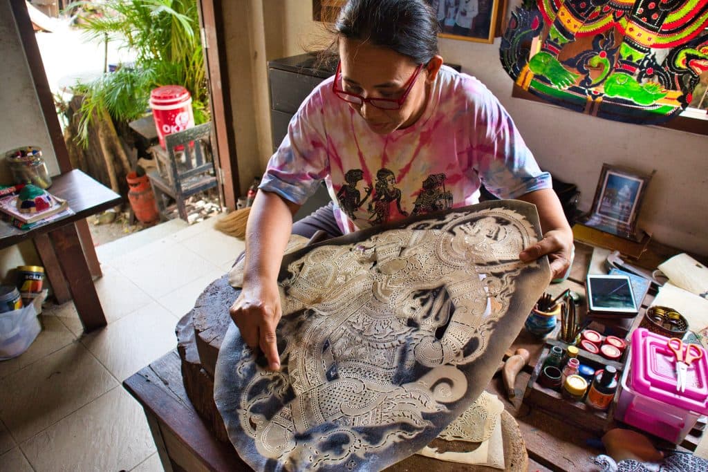 a woman shows how to make a shadow puppet. she is holding a big board with white pattern and points her finger at some of the parts.