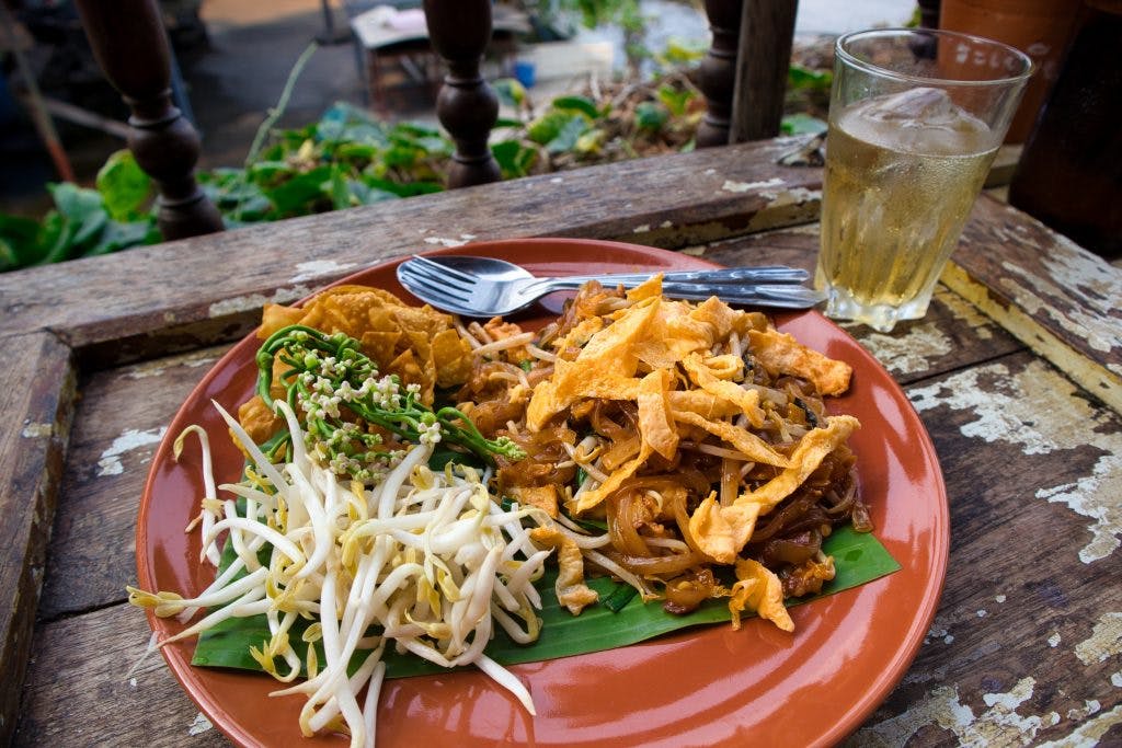 pad thai on a brown plate on a wooden table with soy beans and some egg. Koh Kret, Bangkok. 