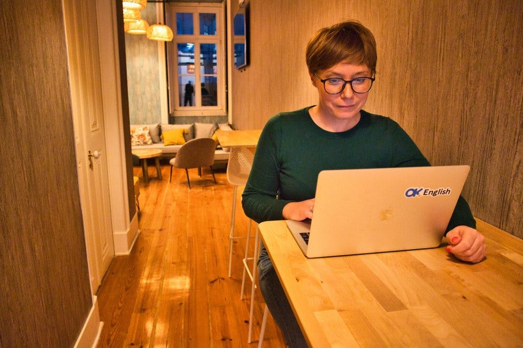 insurance digital nomads. A woman in a green jumper sits in front of a computer in a room.
