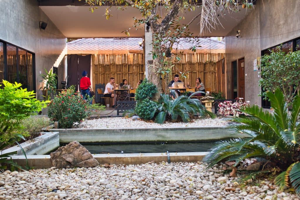A group of digital nomads are working in a small garden with a pond in Chiang Mai, Thailand.