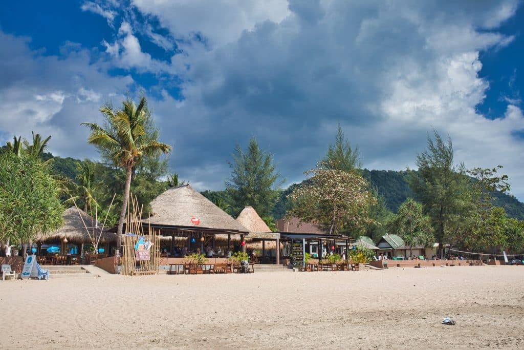 a bamboo hut standing on a beach in koh lanta near the hills and green forest.