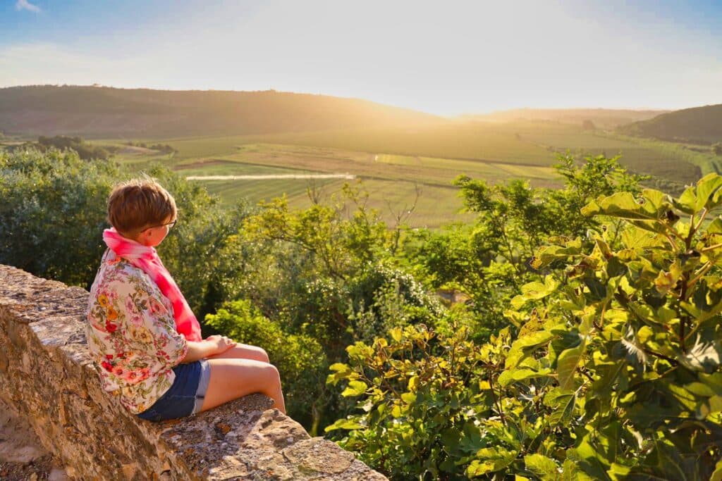 dziewczyna siedzi na murku w portugalii i patrzy sie na zachodzace slonce