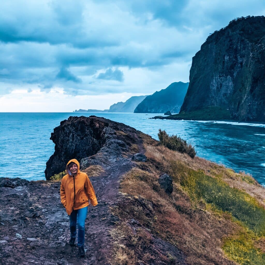 Miraduro do Guidaste, dziewczyna w żółtej kurtce idzie po klifie w deszczowej pogodzie.