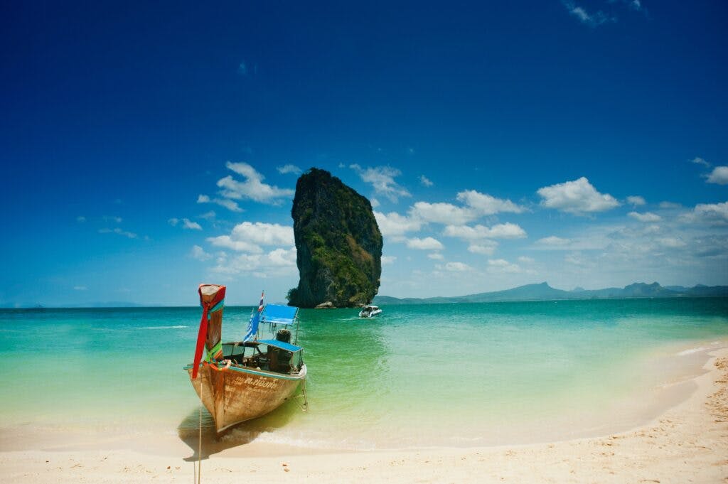 A boat standing at the shore in Thailand in front of a big rock.