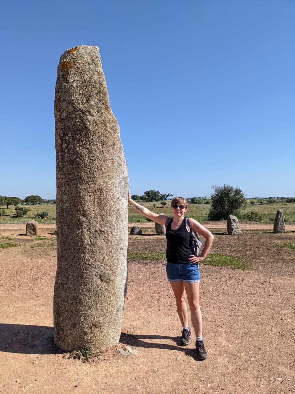 dziewczyna w szortach stoi oparta o wielki glaz w alentejo.