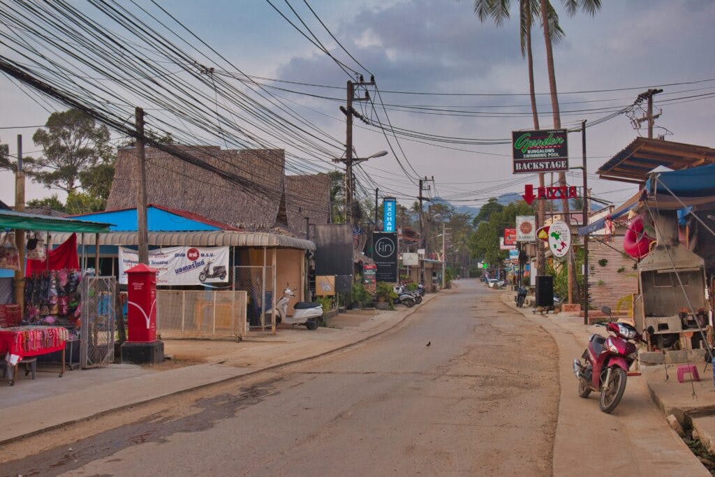 ulica na tajskiej wyspie. Po obu stronach widać sklepy. Przy brzegu stoi motor.