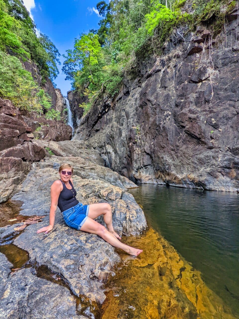 kobieta siedzi na skale nad wodospadem w Tajlandii.