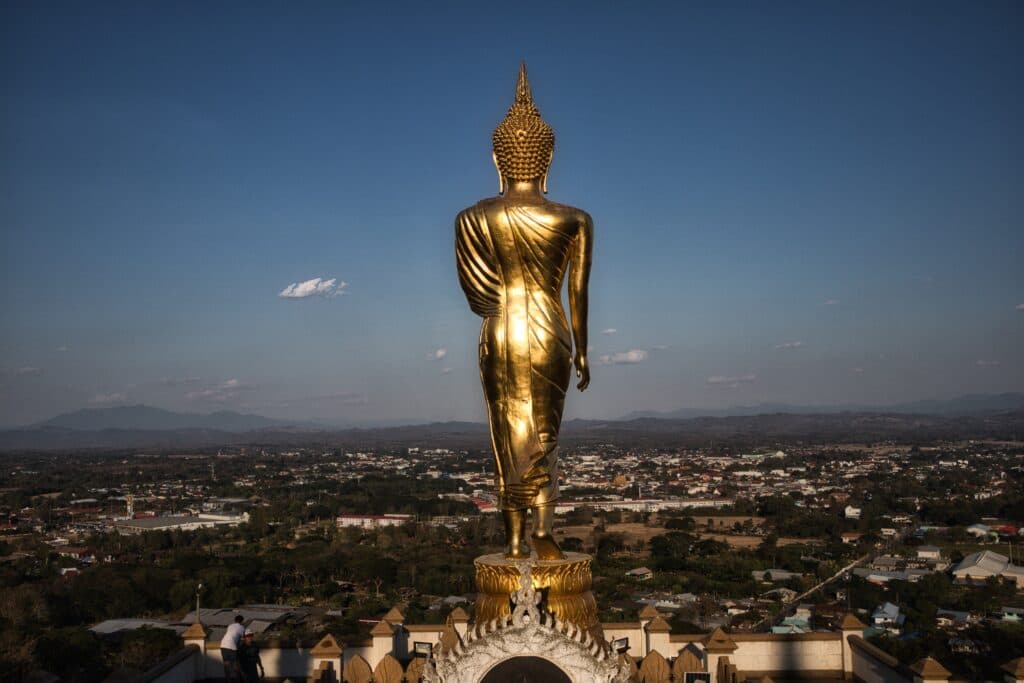 A golden buddha statue stands on a hill in thailand.