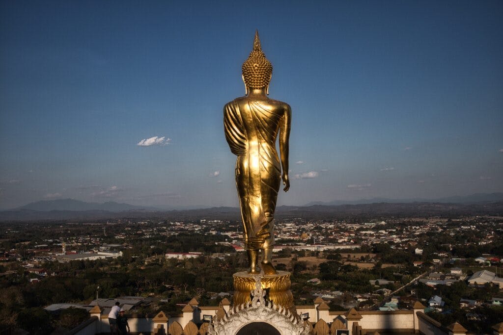 A golden buddha statue stands on a hill in thailand. 
