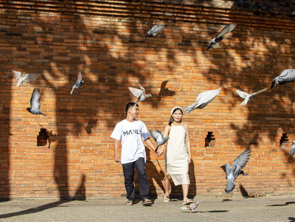 Para trzymająca się za rękę wśród gołębi, Chiang Mai.