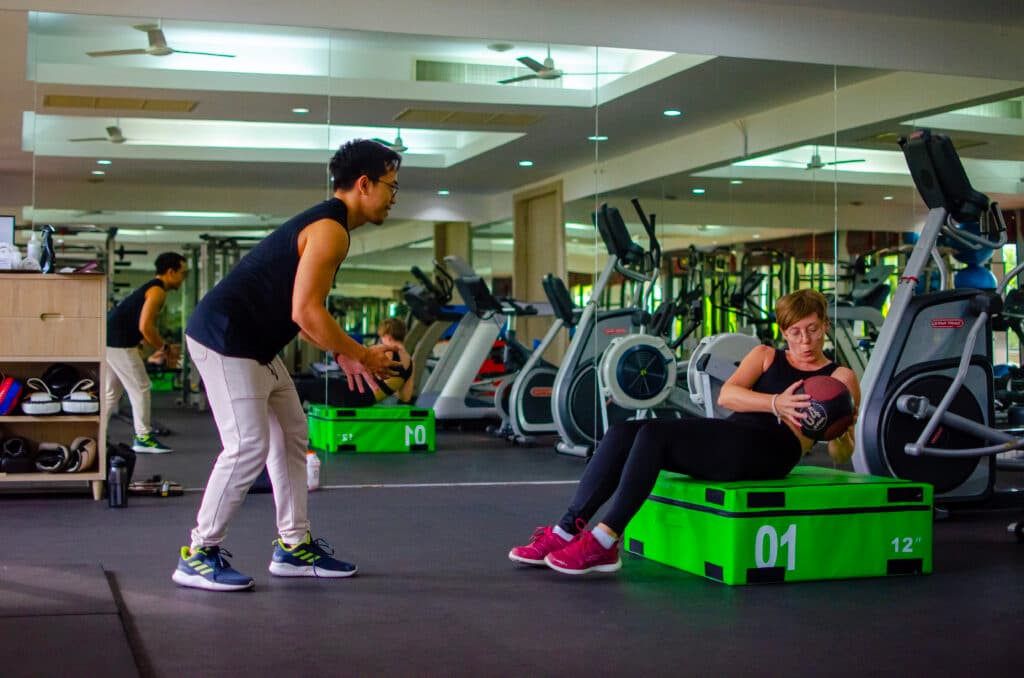 A woman exercising with a ball with a personal trainer at Absolute Sanctuary, Koh Samui.