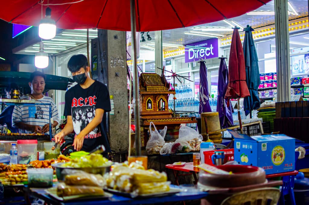 Dwóch młodych Tajów stoi przy stoisku z jedzeniem na Chiang Mai Gate Market.