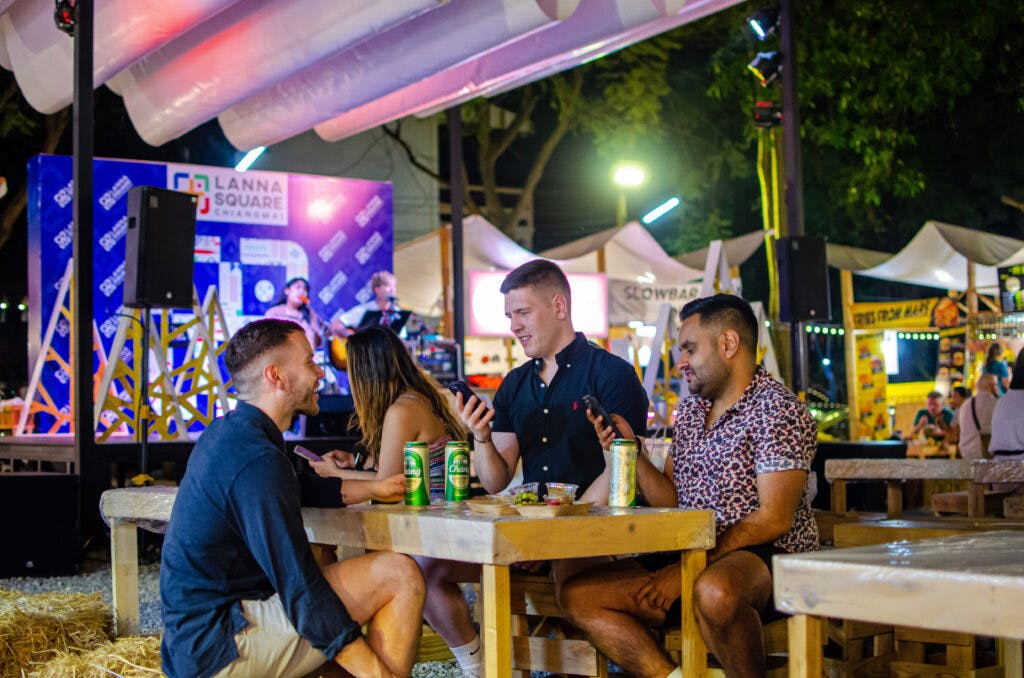 Trzech mężczyzn siedzi przy stole z piwem i patrzy w telefon na markecie w Chiang Mai. 