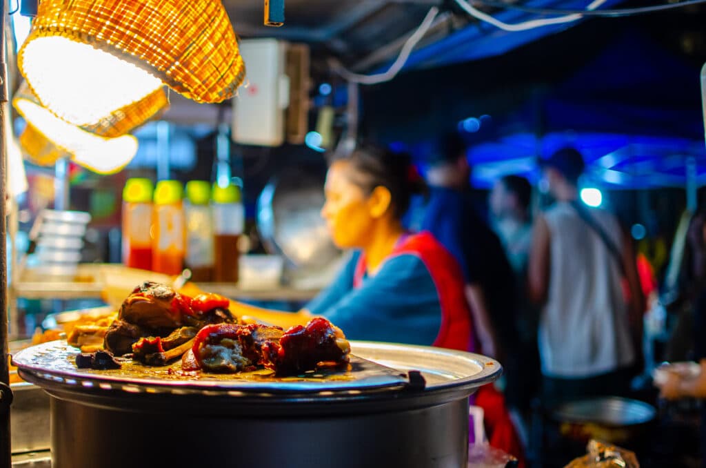 A leftover meat on a plate. Behind we can see a woman seller. Chiang Mai, Thailand.