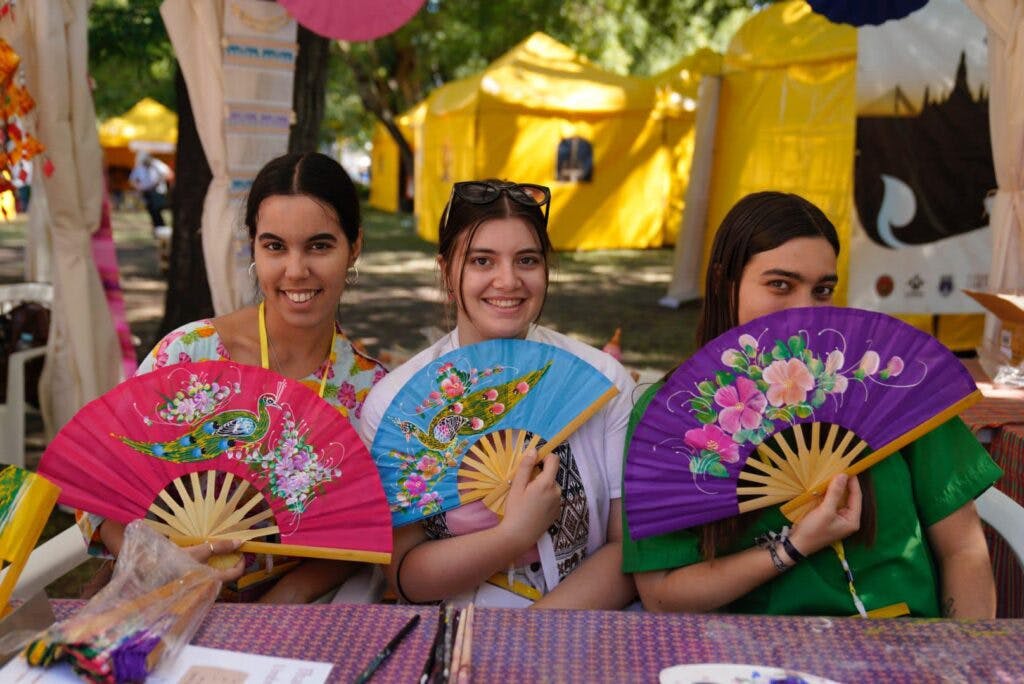 Three girls holding colourful fans at the thai festival in belem, portugal. 