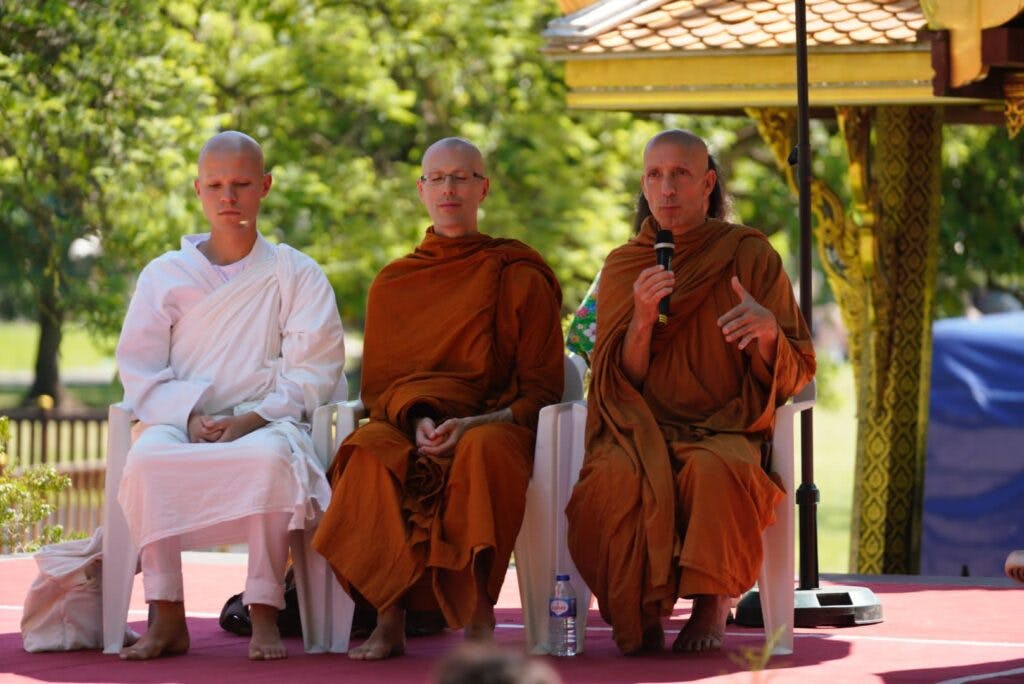 3 monks sit peacefully on chairs on a stage during the thai festival in lisbon. 