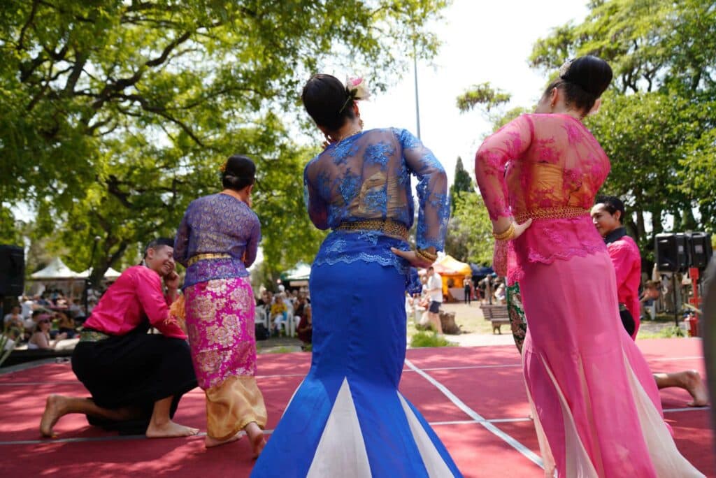 3 ladies dressed in colourful traditional costumes bow on stage at the thai festival in belem, portugal.