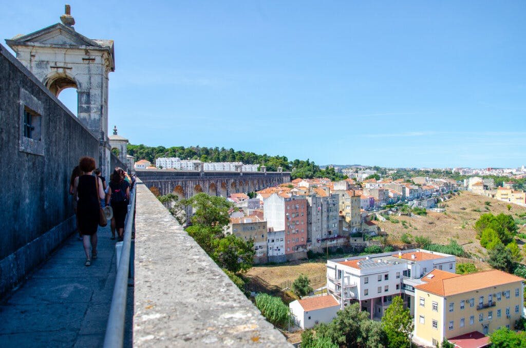 Grupa ludzi idzie po murach akweduktu w Lizbonie. 