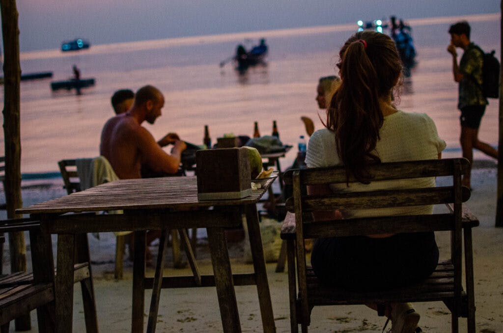Kobieta siedzi przy stoliku na plaży na Koh Tao, w Tajlandii. Zachód słońca. 