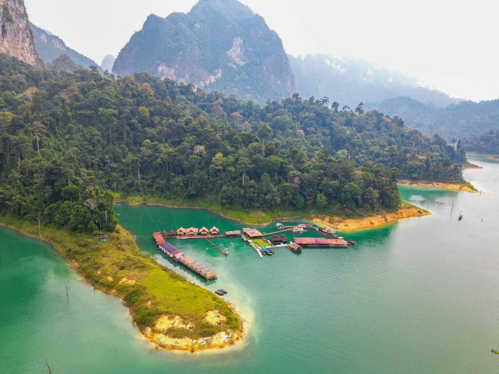 Pływające domki w khao sok na jeziorze widziany z góry, na tle skały, wzgórz i lasu.