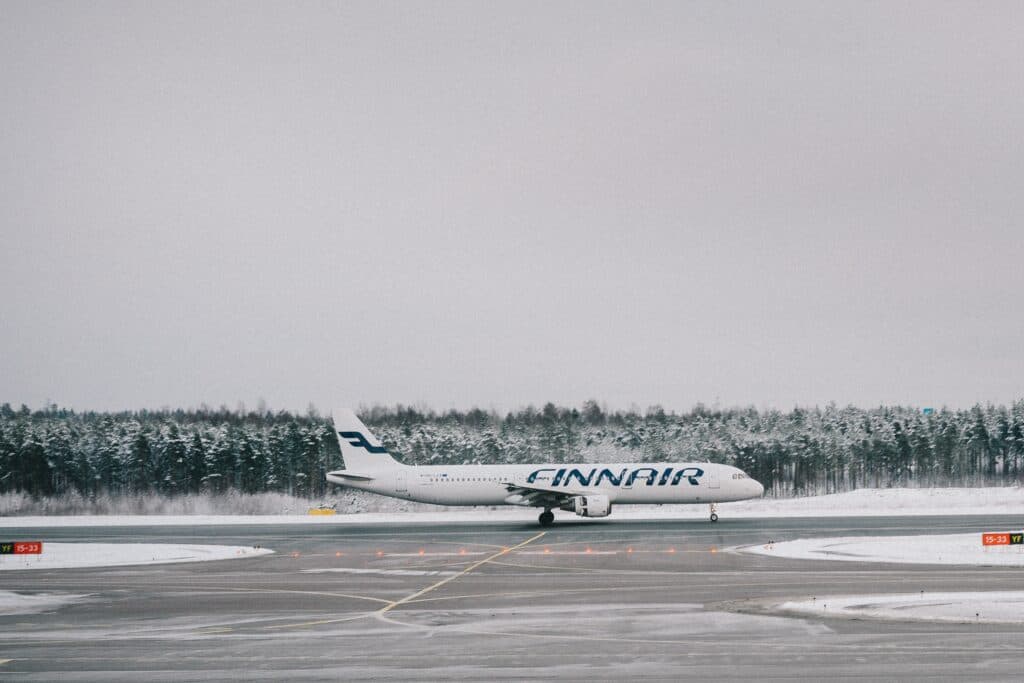 A finnair airplane on a runway in the snow. Behind the plane we see trees covered in snow.