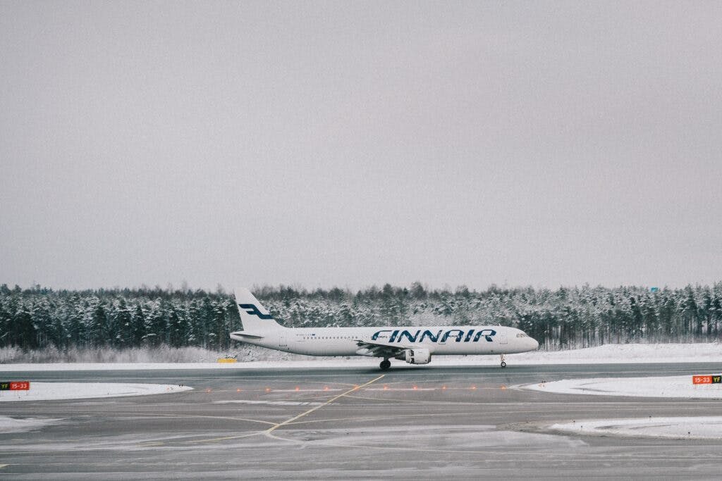 A finnair airplane on a runway in the snow. Behind the plane we see trees covered in snow. 