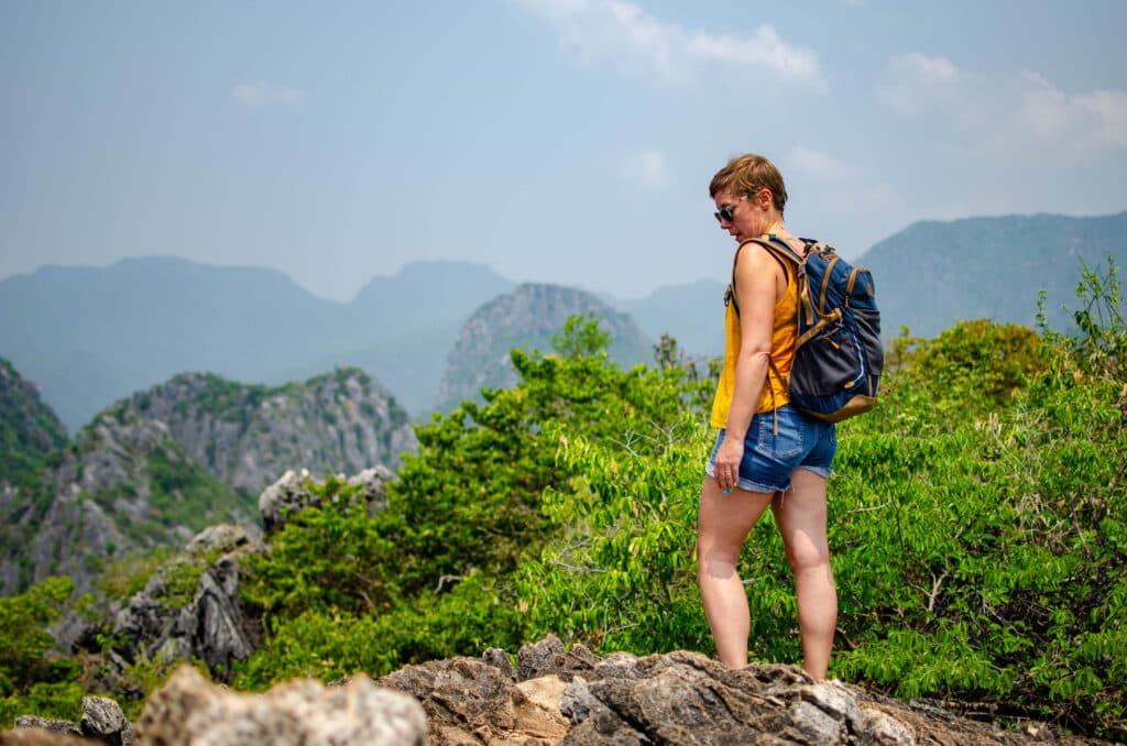A woman in a yellow top stands on the top of the hill in Thailand.