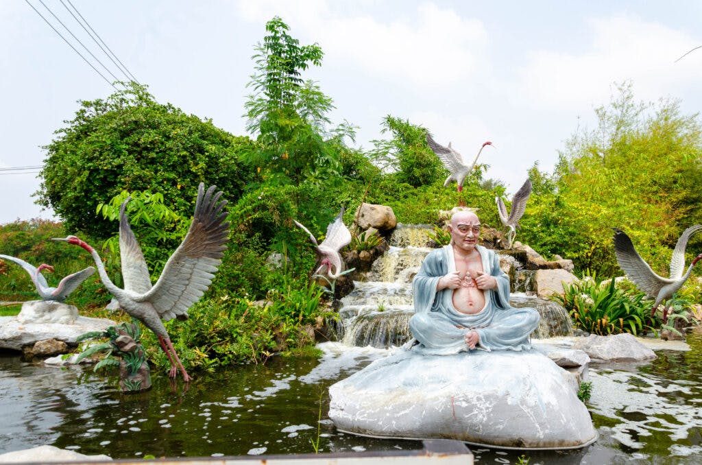 Figura Buddy siedzącego na kamieniu przy wodospadzie w otoczeniu ptaków w Ancient City. 