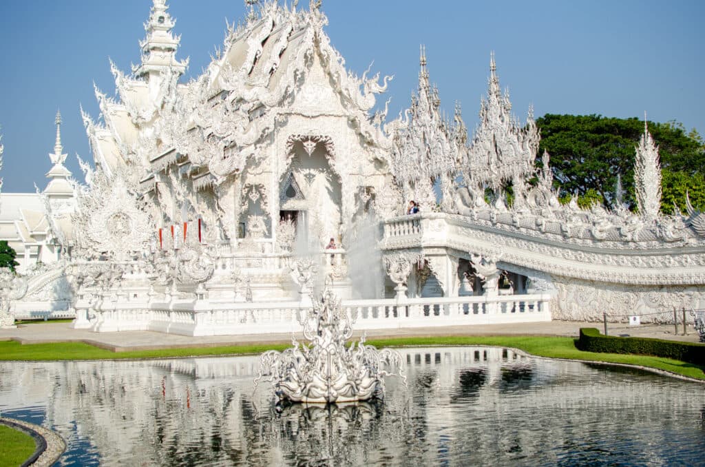 The main building of the white temple in Chiang Rai with a pond outside of it.