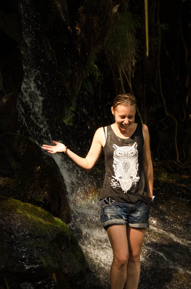 a woman standing under a waterfall in a top and shorts lauhing, in mea hong song, thailand
