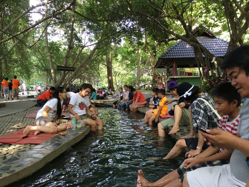 People dipping their legs in warm water from the San Kamphaeng Hot Springs