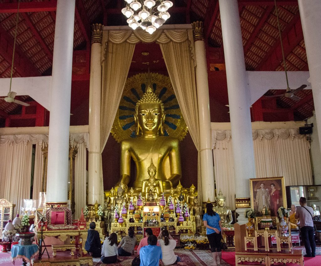 People praying in front of a golden buddha statue inside Wat Phra Singh