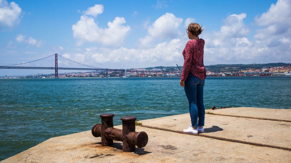 a girl standing in almada looking at the bridge in lisbon