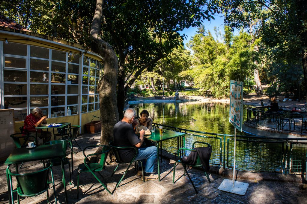 people sitting in a cafe near the pond in the estrela park, lisbon