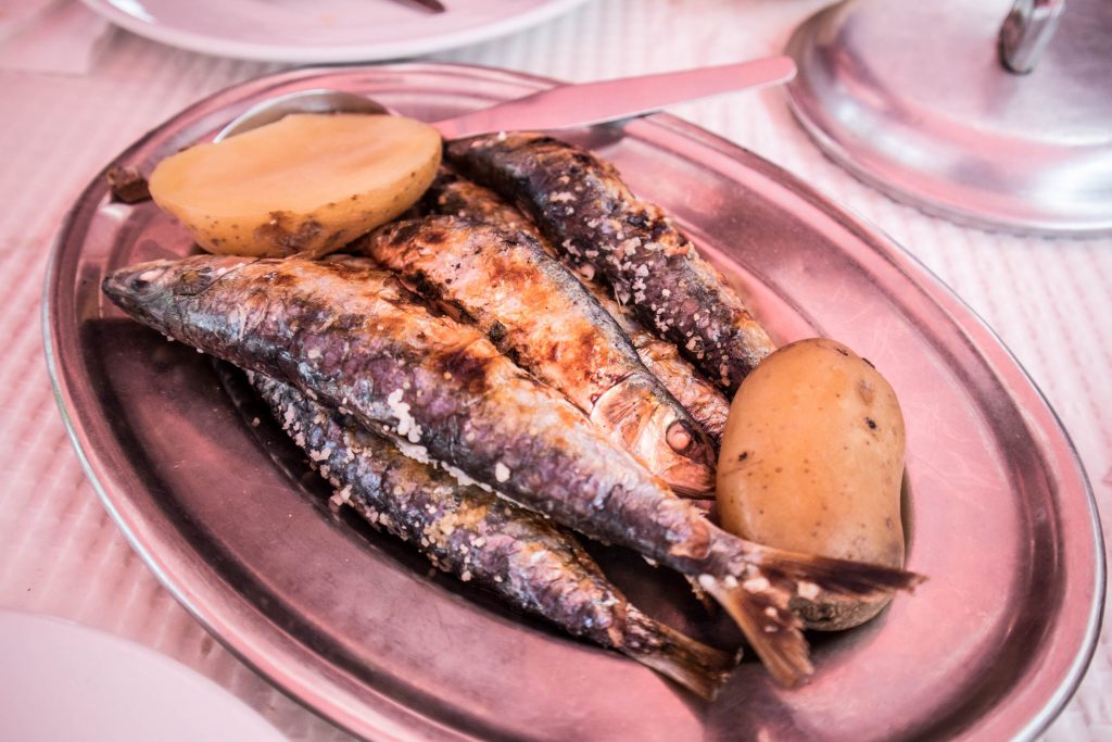 rozowy talerz z grilowanymi sardynami i ziemniakami na stole w restauracji cacilhas