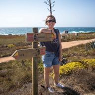 a girl stands at the shore near guincho beach at the road signs pointing directions