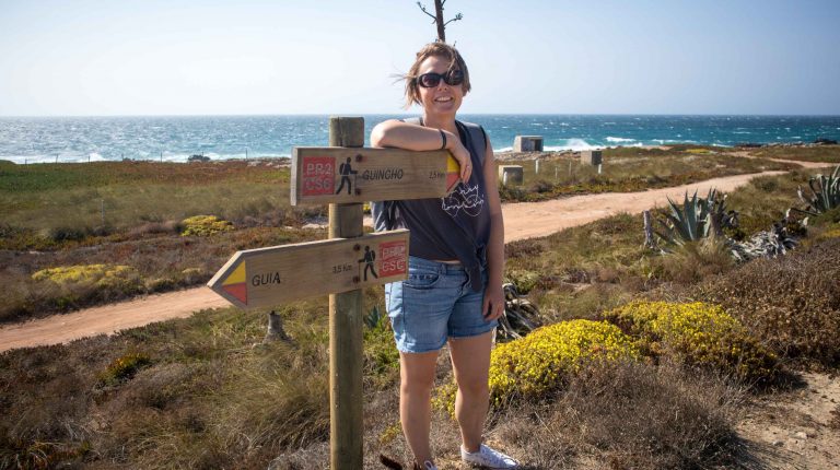 a girl stands at the shore near guincho beach at the road signs pointing directions